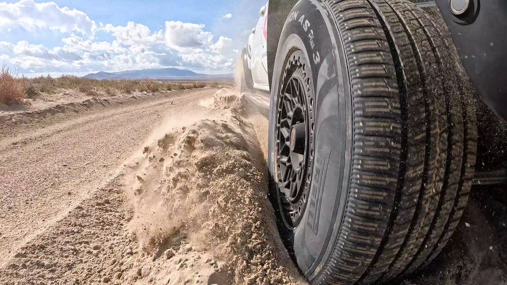 Pirelli Scorpion AS Plus 3 som kastar upp lös sand bredvid en Ford Ranger Raptor