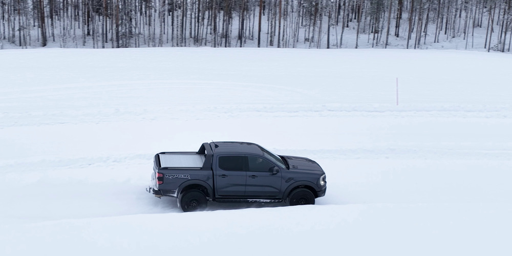 Grå Ford Ranger Raptor som kör över en snötäckt testbana bredvid en skog